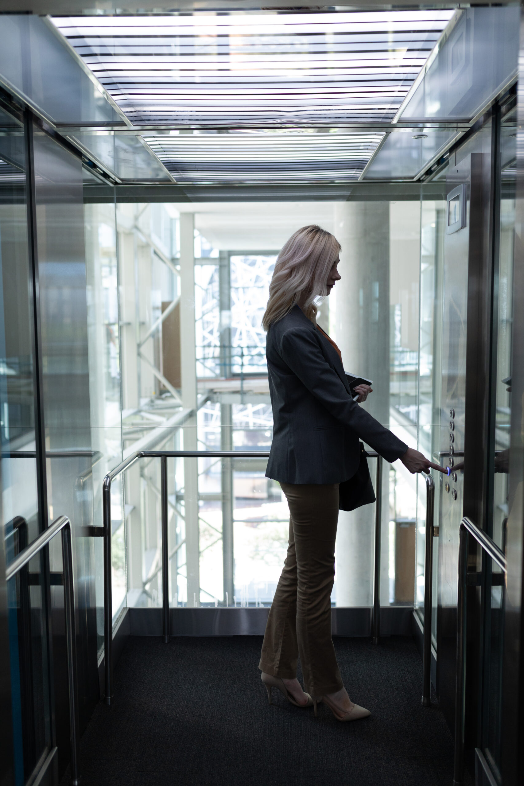 Side view of pretty young blonde Caucasian businesswoman using elevator in modern office